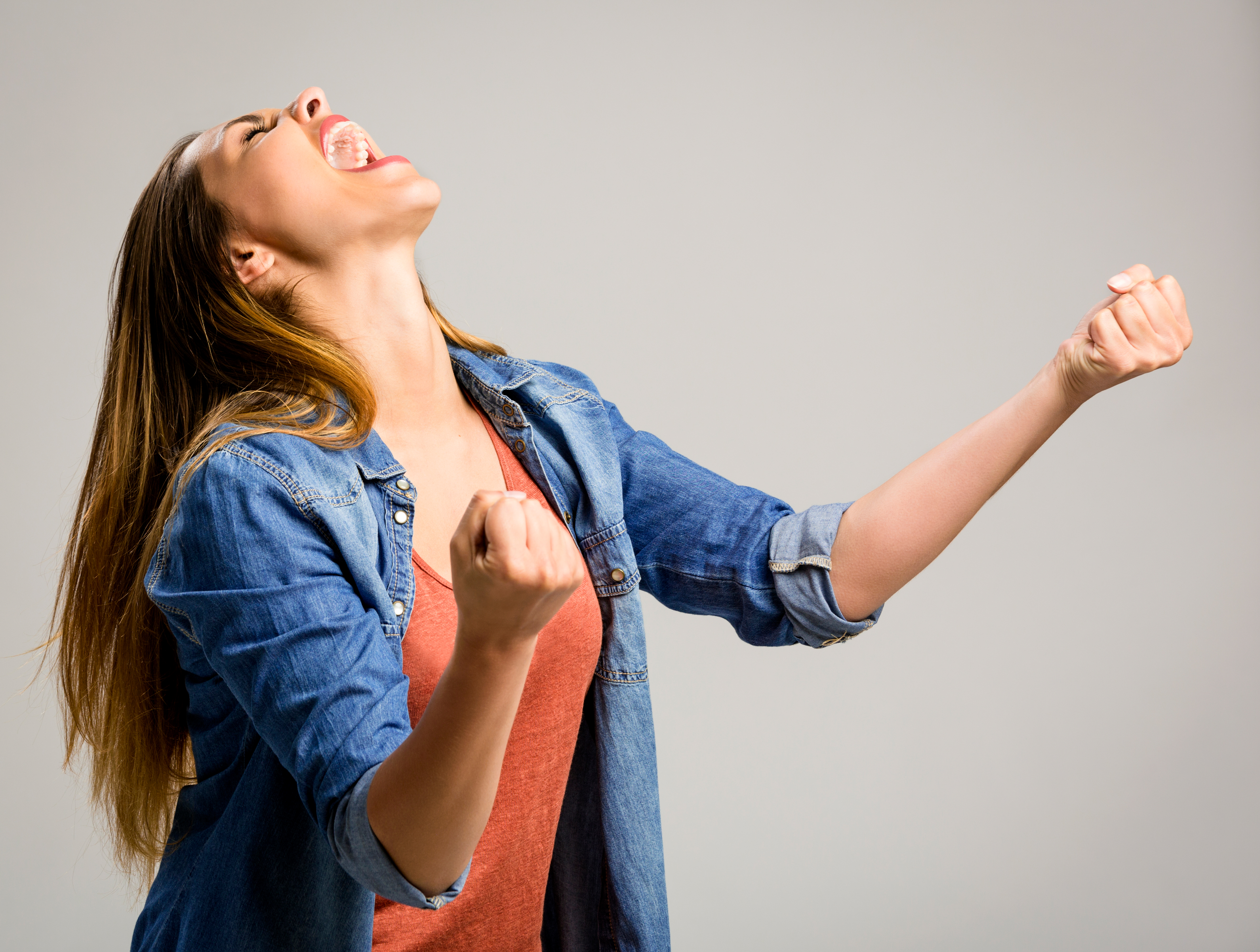 Beautiful happy woman with arms up over a gray background