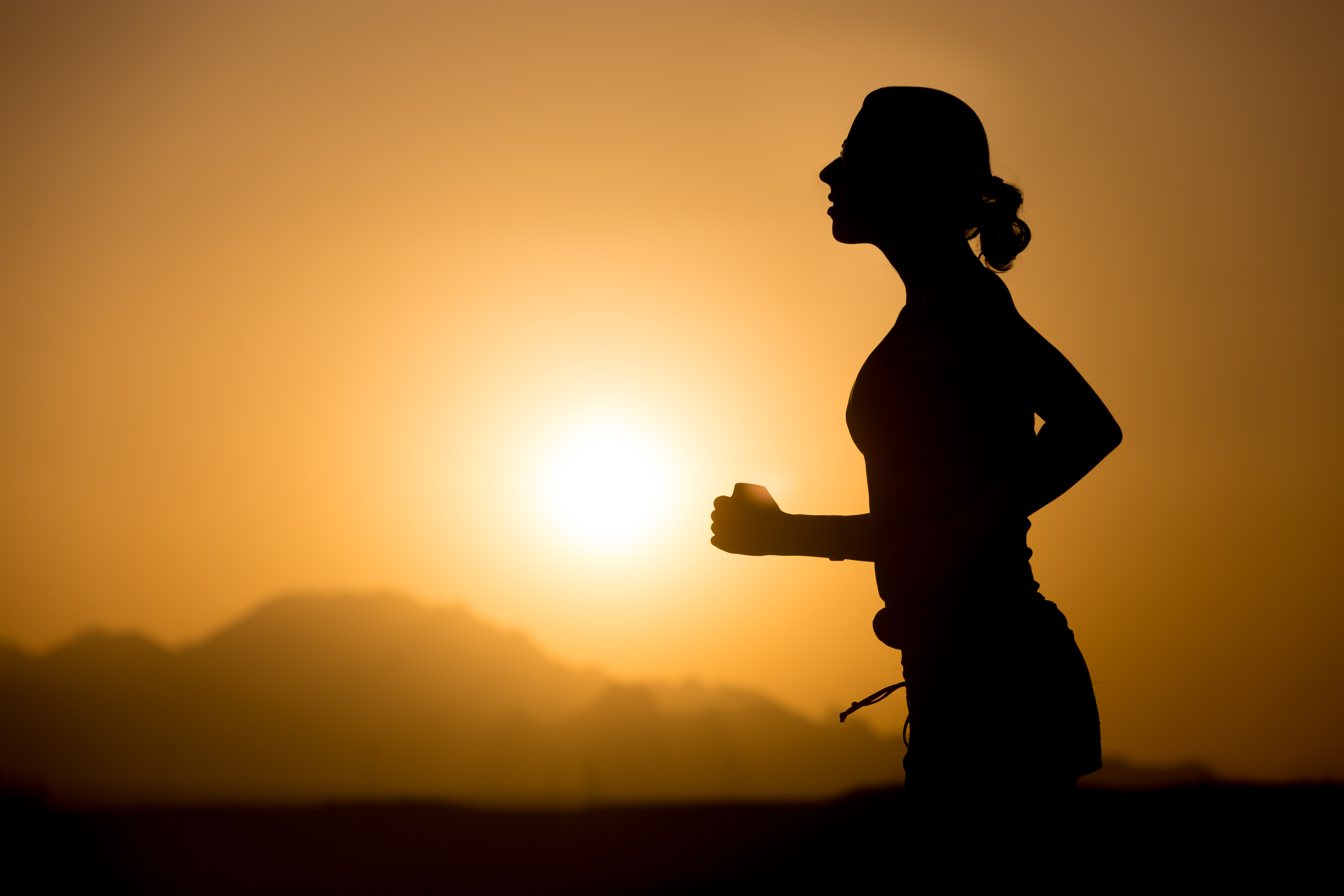 Profile silhouette of young sporty woman jogging against colorful picturesque mountainous landscape with rising or setting sun, copy space